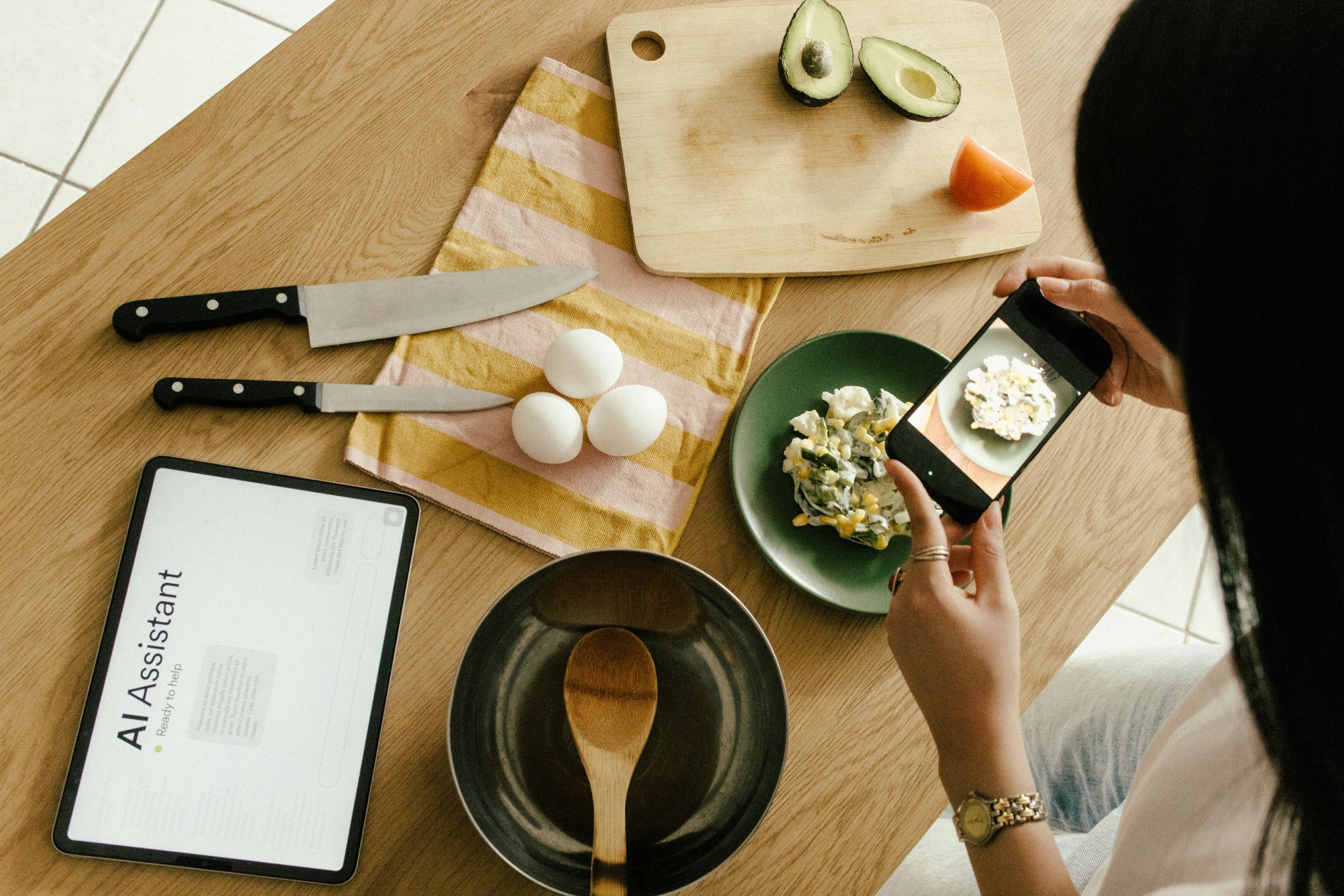 A person photographing a home-cooked meal beside a tablet showing an AI assistant